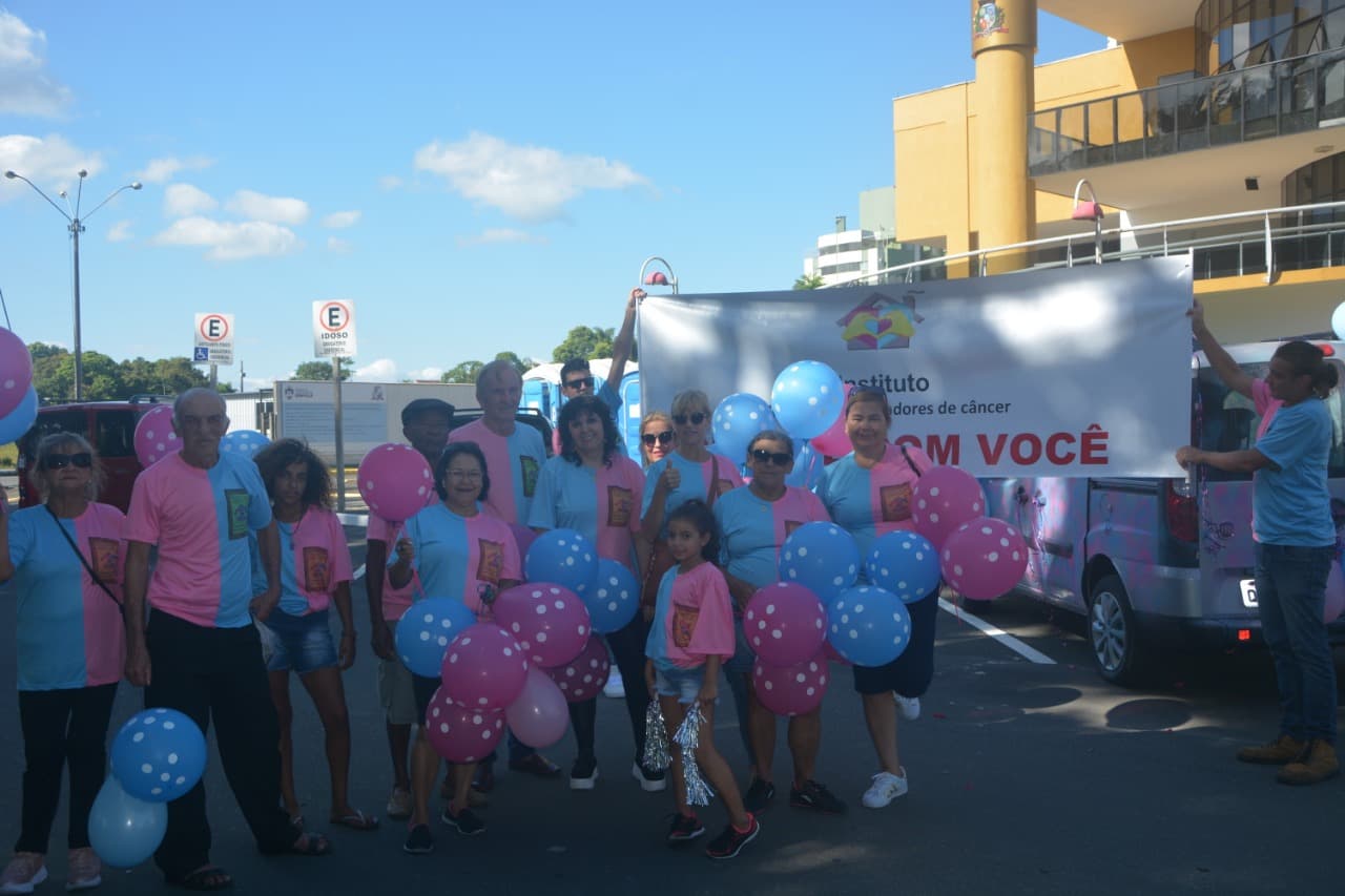 Voluntários e pacientes posando com faixa e balões antes do desfile